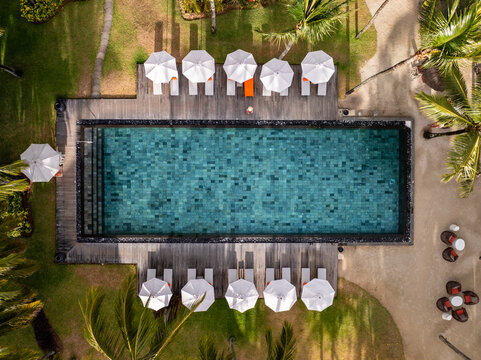 Aerial view of turquoise waters of a rectangular pool contrasting with the white umbrellas and wooden deck, Prince Maurice, Flacq District, Mauritius.