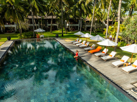 Aerial view of a serene pool reflecting the lush palms, contrasted by the vibrant loungers, Prince Maurice, Flacq District, Mauritius.