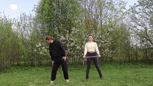 A young couple doing sports outdoors, gymnastics and physical education exercises with a rubber band
