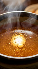 Intense close-up reveals rising steam and golden oil bubbles floating on the surface of a rich, dark brown soup.