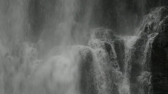 Close up view of black wet cliffs covered by cascades of a large waterfall.