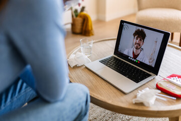 Sick Caucasian woman talking to doctor online using laptop at home. Patient having video call...