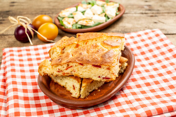 Pieces of homemade bread with onions served in an earthenware bowl on a wooden table, with salad and fresh vegetables on the side.