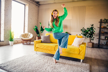 Naklejka premium Young woman in a green sweatshirt cheerfully dancing in a vibrant loft style living room during a sunny day indoors