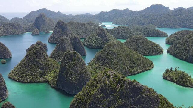 Low angle aerial drone flight over Wayag Island karst formations in Raja Ampat. Close up view of lush limestone cone-shaped islets and turquoise sea water in Indonesia