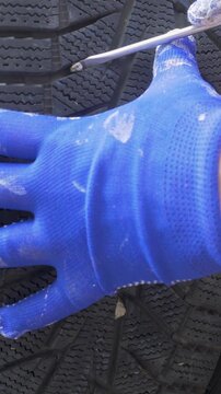 Man worker hand in work gloves checks tire tread and takes out gravel before frost arrives. Winter grip requires open pattern. Proper preparation avoids skids and accidents