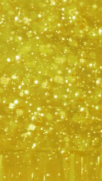 Small bubbles are scattered in yellow liquid, creating shimmering effect. The varying bubble sizes give the liquid a fizzy look, similar to a science experiment