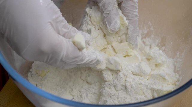 Hands covered with gloves mix ingredients for biscuit crust. Flour and butter merge perfectly. Texture stays light yet firm for baking