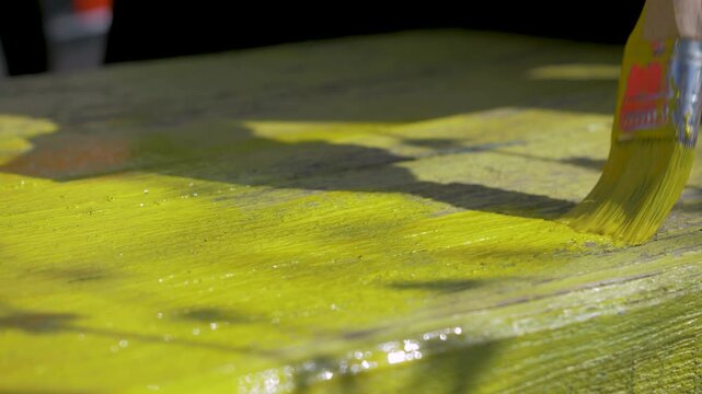 Seasonal garden setup starts with brush loaded in yellow paint. Female renovator colors wood with care. Calm background emphasizes hands-on creativity in natural environment