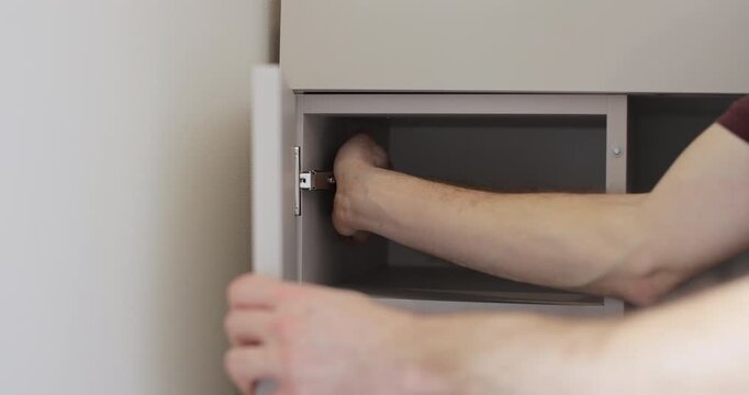 Furniture assembler works on cabinet door hinge in flat. Installation of new furniture. Furniture installation.