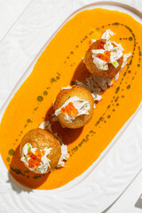 Golden fried crab croquettes topped with red caviar served on creamy orange sauce in elegant...