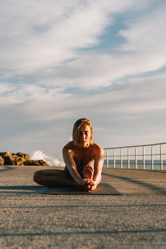 Woman practicing yoga janu sirsasana pose outdoors by ocean