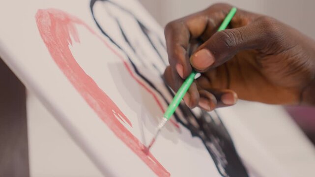 Black artist painting canvas closeup brush strokes, dark skinned hand tracing pink curve around black silhouette on tilted canvas, studio table, acrylic texture visible, focused steady motion