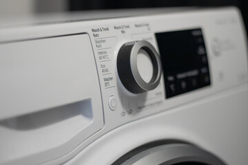 White washing machine control panel featuring various settings and a large dial for selecting wash cycles, with a digital display showing options and temperatures