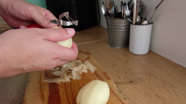 Man uses peeler to peel potatoes at kitchen counter, closeup food prep