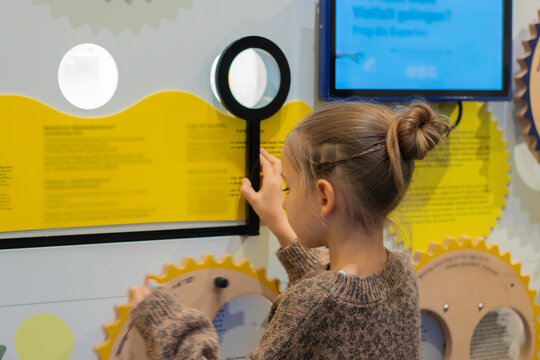 Child interacting with an educational exhibit in an interactive museum, examining information through a magnifying glass on a colorful display
