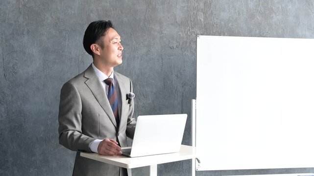 ピンマイクをつけてプレゼンをするスーツの日本人男性
