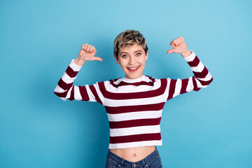 Young woman with short blonde hair wears a striped sweater and smiles while posing with arms raised...