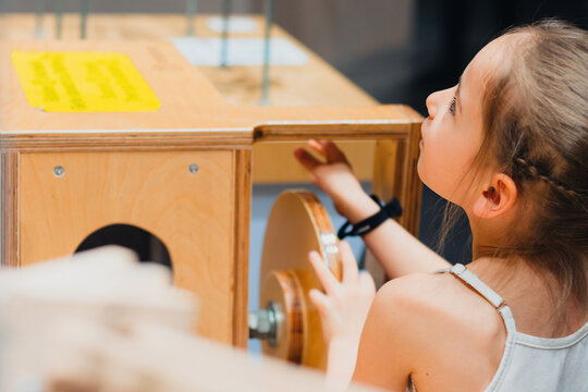 Young girl interacting with a wooden educational exhibit featuring gears and levers inside an interactive museum space designed for childrens learning and exploration