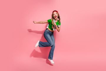 Joyful young woman jumps on pink background wearing a green top jeans and red cap