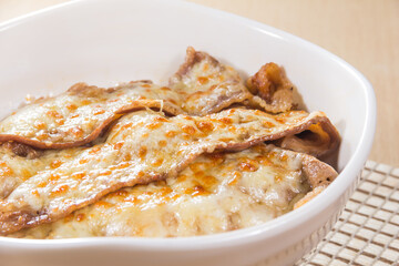 A white ceramic dish filled with rice and beef slices covered in melted golden cheese.