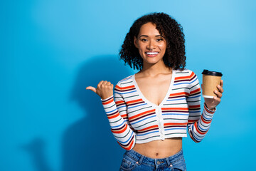 Young chic woman in striped cardigan smiles with coffee cup on blue background for lifestyle...
