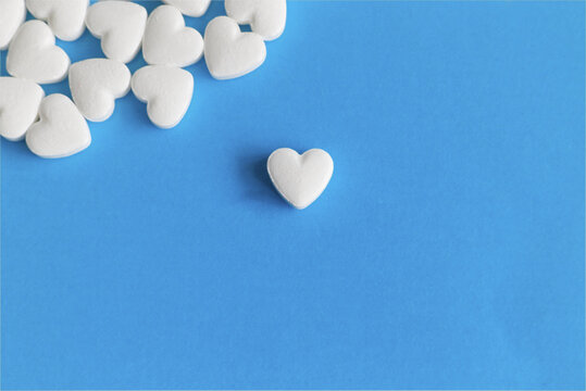 A single white heart-shaped pill in the center of the frame with a group of pills in the upper corner, symbolizing conscious drug choice and reliable supply for cardiovascular treatment courses.