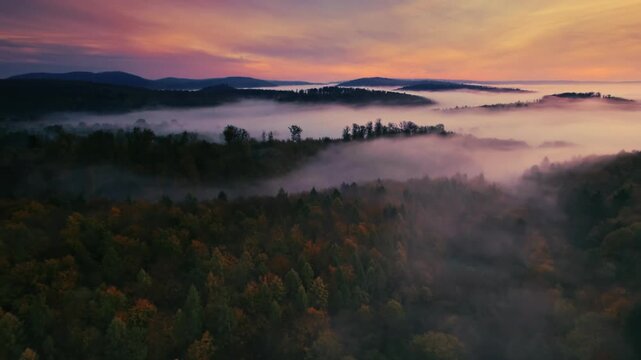Gorgeous colorful dawn with orange clouds and mist over a landscape with hills and forests in autumn, aerial panning view