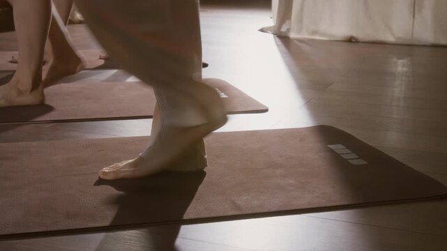 Medium lockdown floor level shot of three young female yoga practitioners in sportswear rolling out mats in turn in loft studio, walking forward, suggesting togetherness and active lifestyle