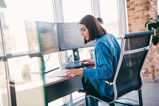 Businesswoman coding at a modern loft office with dual monitors and a focused freelancer at workstation