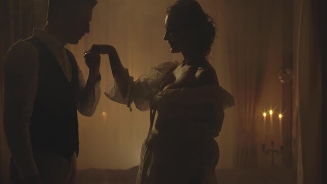 Black silhouette happy couple lady curtsies, gentleman kisses female hand. king greets queen victorian white dress. Night dark room candles light. Adult girl with man, love old style medieval ball 4k.