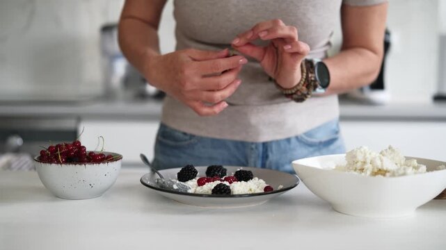 Woman Adds Red Viburnum Berries To Cottage Cheese On A Plate In The Kitchen