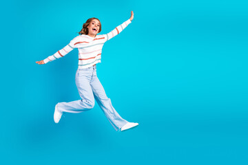 Fototapeta premium Joyful woman leaps in the air wearing a striped sweater and jeans against a bright blue background for a vibrant lifestyle and fashion themed stock image