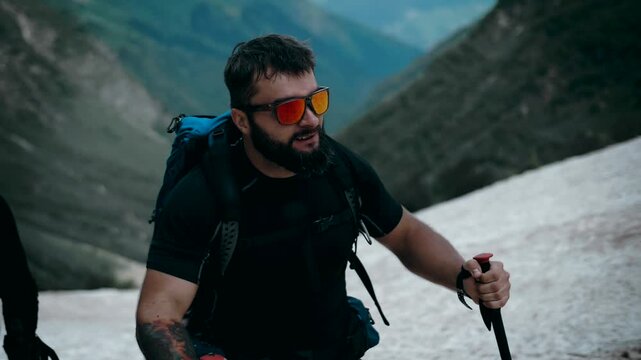 Mountaineer with a beard moves to the top of the snow-capped mountains in the snow of the glacier. Super Slow-motion shot.