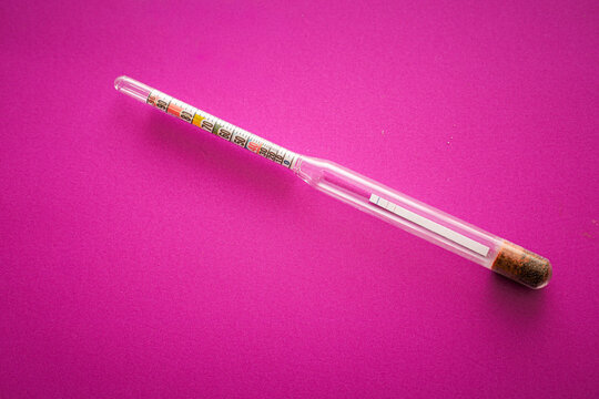 ​A glass household hydrometer with a bright colored scale is positioned diagonally on a rich purple background.