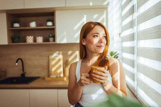 Smiling Woman Enjoying Morning Coffee in Bright Kitchen Bathed in Natural Sunlight