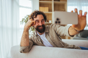 Fototapeta premium Bearded Man Taking Selfie On Couch At Home Smiling Relaxed Lifestyle And Happiness