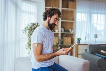 Man Using Smartphone to Check Glucose Monitor at Home, Managing Diabetes With Wearable Sensor
