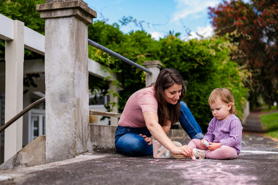 Mum and toddler daughter sitting on a pavement making drawings with colourful chalk