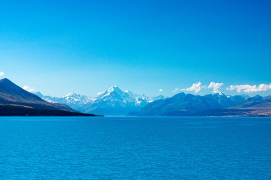 looking across a blue lake with blue snow capped mountains in the distance and blue sky