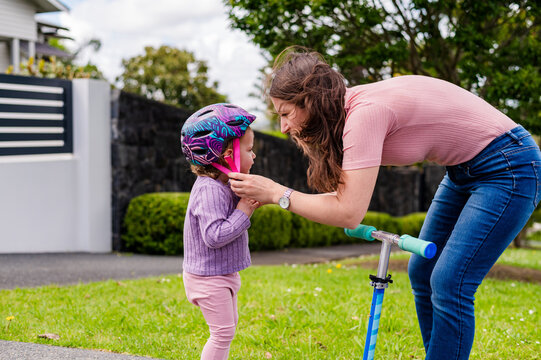Mum securing toddler daughters helmet before riding the scooter outdoors