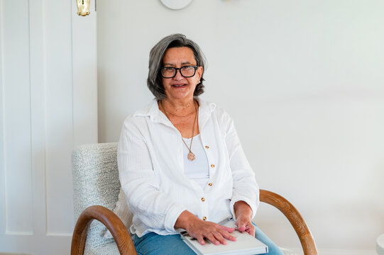 Senior woman sitting on a chair in a modern room while holding a book