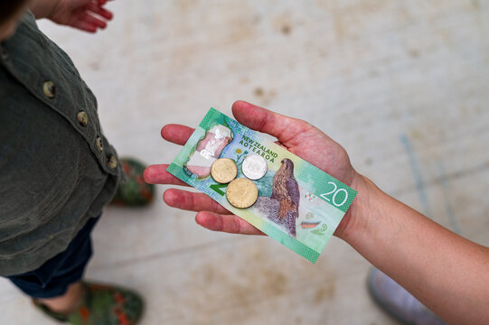 Adult hand handing out New Zealand dollars to toddler boy