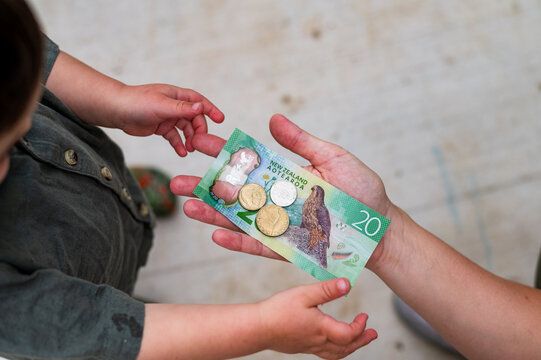 Adult hand handing out New Zealand dollars to toddler boy