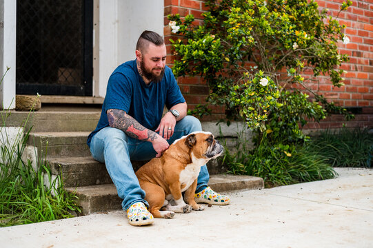 Man pets bulldog while sitting on steps in front of house in New Zealand