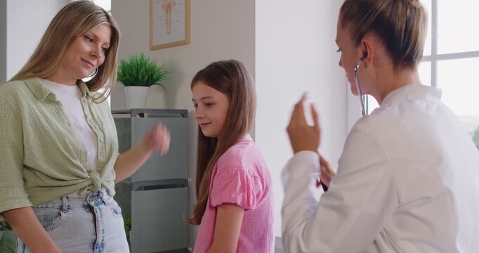 Pediatrician using stethoscope on girls back to examine lungs during routine examination in modern clinic. Auscultation checkup on healthcare consultation for child, doctor listening to kids breathing