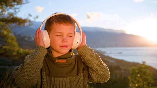Boy relaxing with audio content during sunset. Theme of mental health, stress relief, sensory processing, digital entertainment, and peaceful childhood emotions.