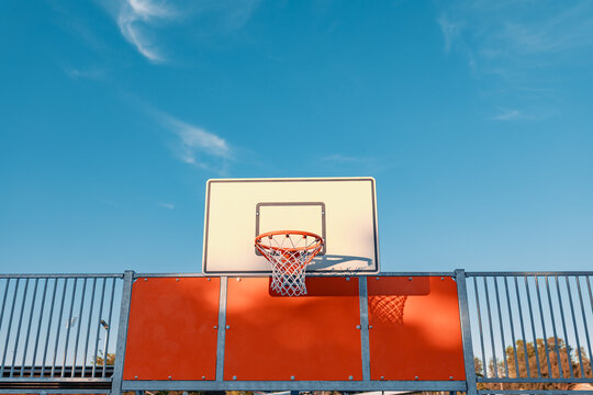 Basketball hoop and backboard illuminated by the setting sun with blue sky