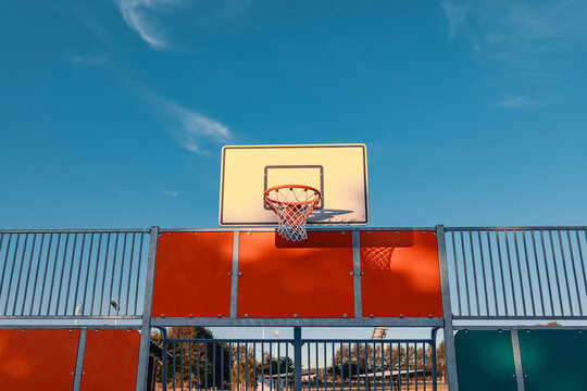 Basketball hoop and backboard at public court illuminated by the setting sun with blue sky
