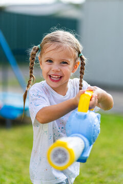 Happy little girl holding bubble blower in backyard during water play fun